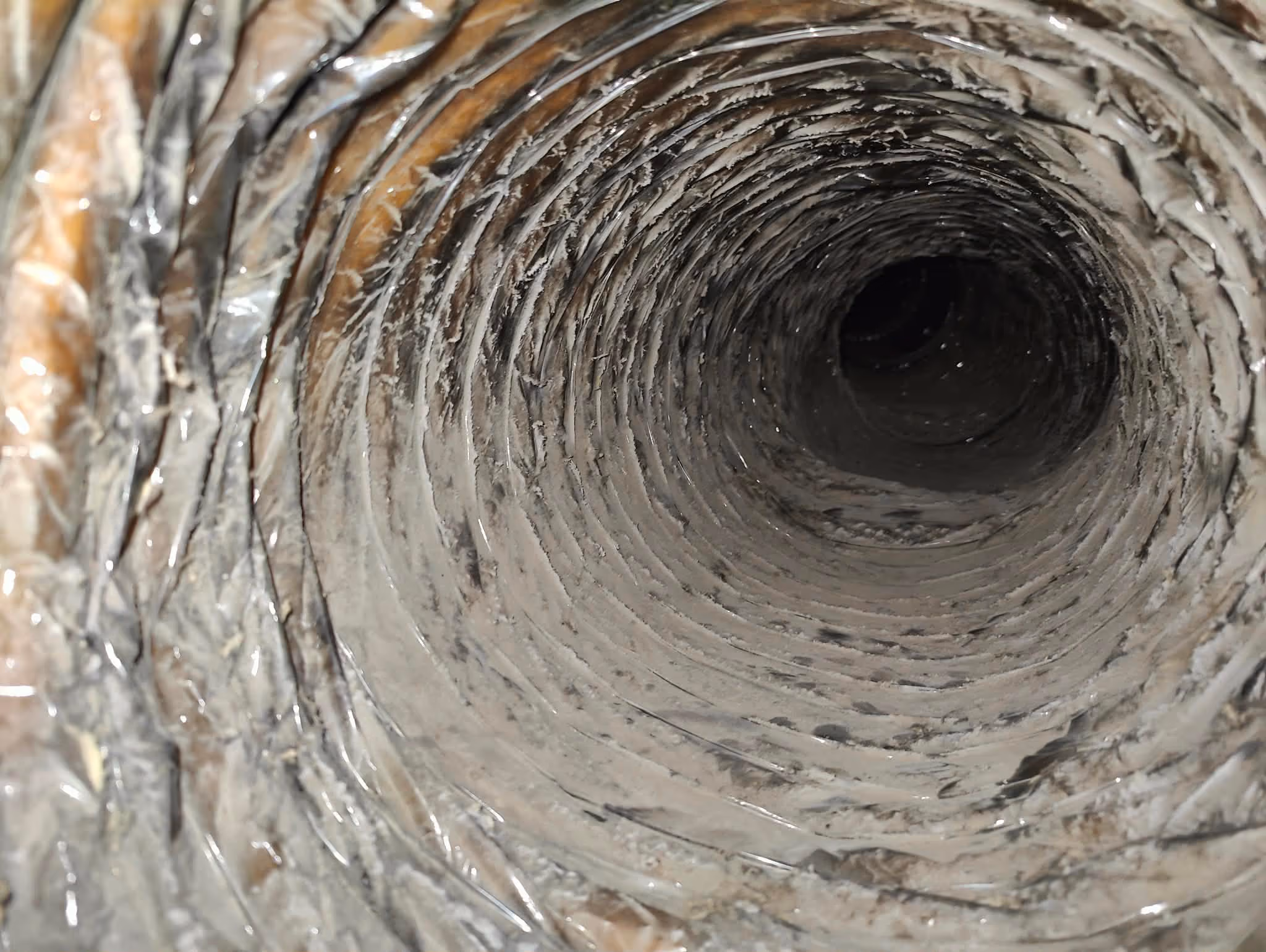 Close-up view inside a dusty, coiled metal duct or pipe.