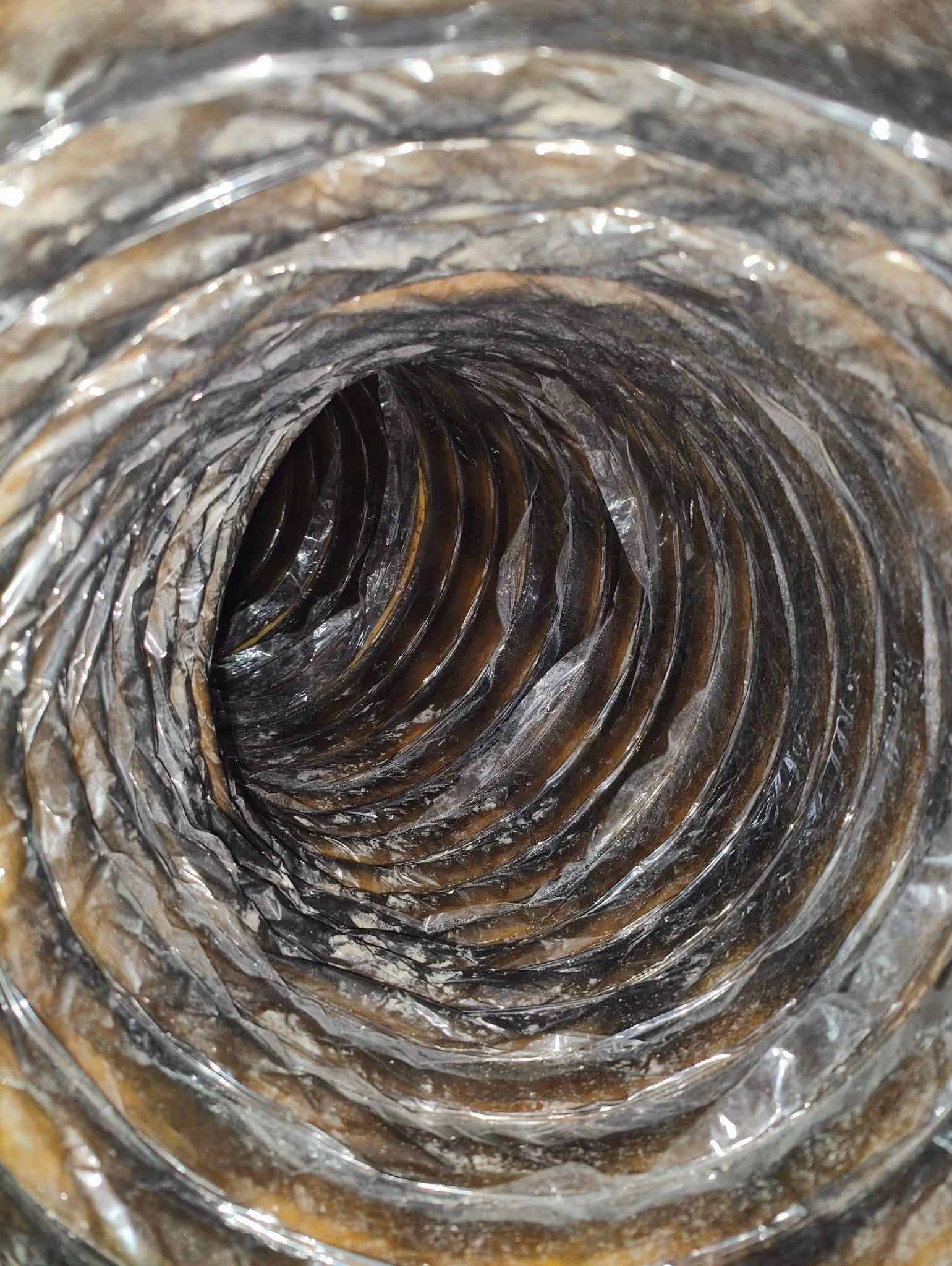 Close-up view inside a flexible metallic ventilation duct with spiral ribs.