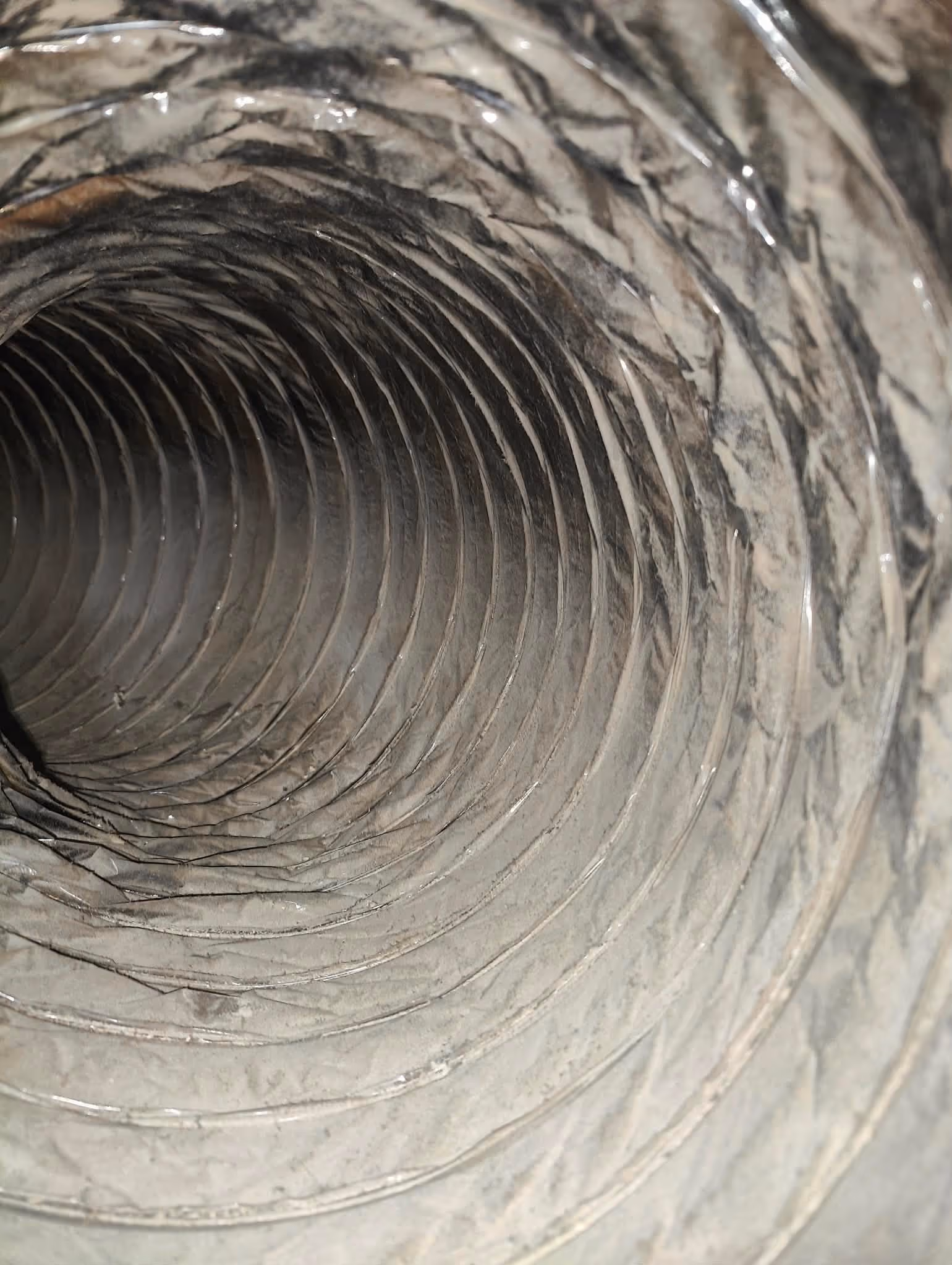 Close-up view inside a flexible metallic duct with a ribbed spiral structure.