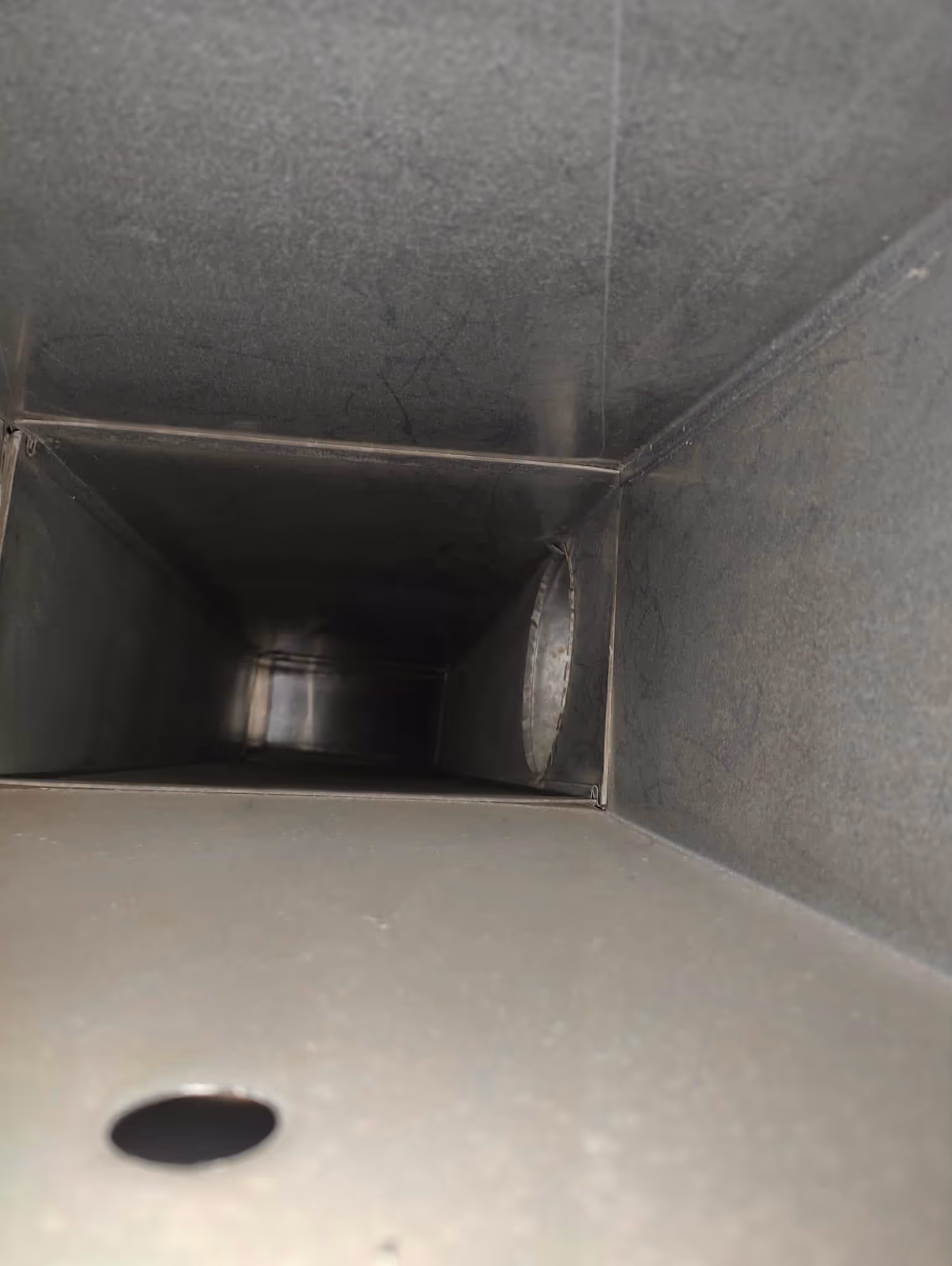 Inside view of a rectangular metal ductwork with a circular hole on the right side wall.